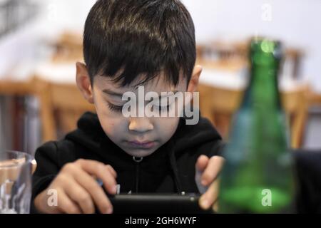 Brunette kleinen Jungen in einer Bar beobachten ein Video auf einem Smartphone, horizontal. Selektiver Fokus Stockfoto