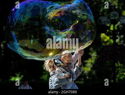 Kiew, Ukraine. September 2021. Eine Frau trägt ein Kind, um ihn dazu zu bringen, eine riesige Seifenblase im Park zu berühren. (Foto: Sergei Chuzavkov/SOPA Images/Sipa USA) Quelle: SIPA USA/Alamy Live News Stockfoto