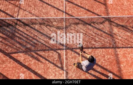 Blick von oben auf einen Paddle-Tennisspieler, der mit dem Schläger auf einem Platz im Freien in der Nähe des Netzes steht. Stockfoto