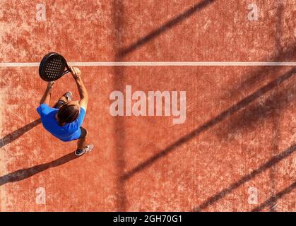 Blick von oben auf einen professionellen Paddle-Tennisspieler, der gerade mit dem Schläger den Ball getroffen hat. Padel Match auf einem Platz im Freien. Stockfoto