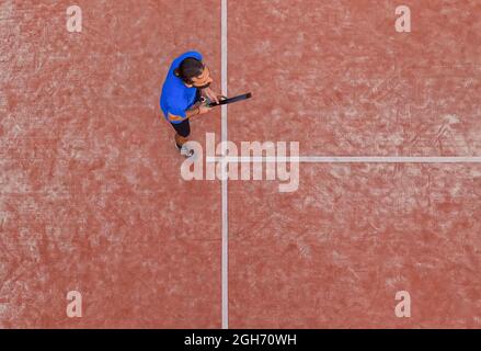 Blick von oben auf einen Paddle-Tennisspieler, der bei einem Spiel auf einem Platz im Freien auf den Ball wartet. Stockfoto