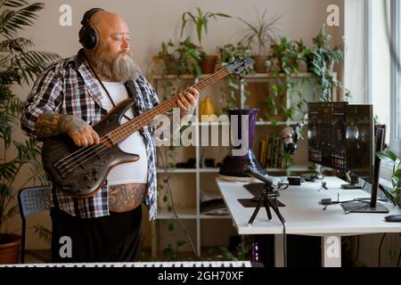 Reifer Komponist spielt am Arbeitsplatz im Heimstudio Basgitarre-Aufnahmen Stockfoto