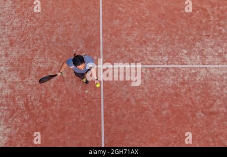 Draufsicht auf einen Paddle-Tennisspieler, der den Ball für einen Aufschlag auf einem Platz im Freien hüpft. Stockfoto