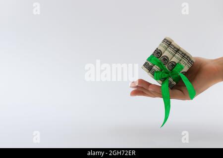 Weibliche Hand hält rollte 100-Dollar-Banknoten mit grünem Geschenkband gebunden. Stockfoto