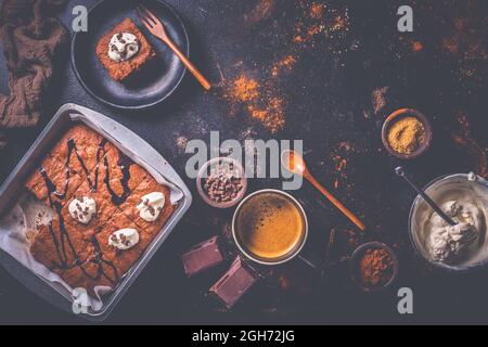 Hausgemachte Brownies mit einer Tasse Kaffee und Backzutaten auf braunem Hintergrund Stockfoto
