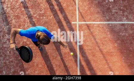 Draufsicht auf einen Paddle-Tennisspieler, der den Ball für einen Aufschlag auf einem Platz im Freien hüpft. Stockfoto