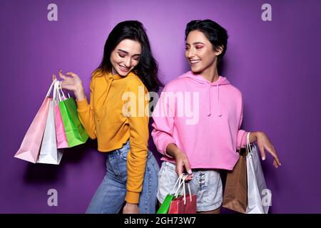 Zwei glückliche Mädchen Freunde Einkäufer halten Einkaufstaschen auf lila Hintergrund. Stockfoto