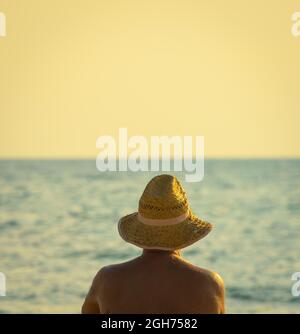 Ein nicht erkennbarer älterer Mann trägt Strohhut und Sonnenbaden am Meeresstrand Stockfoto