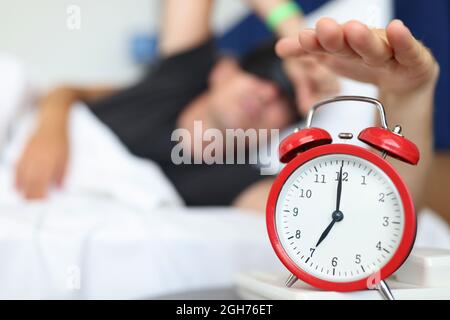 Ausgeruhter Mann greift nach der Uhr-Taste, um den täglichen Alarm auszuschalten und aufzuwachen Stockfoto