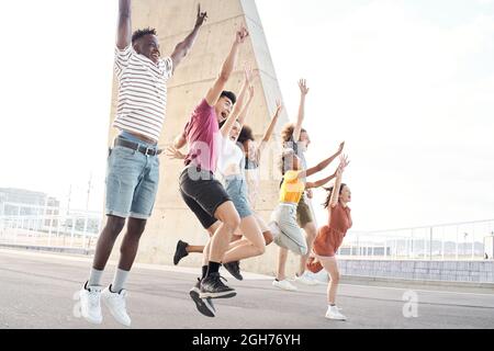 Seitenansicht Porträt einer Gruppe glücklicher multiethnischer Freunde, die Spaß haben. Junge Studenten springen außerhalb der Universität. Stockfoto