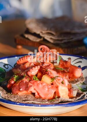 Rote Tintenfisch-Ceviche auf blauen Mais-Tostadas, mexikanisches Fischgericht aus Baja California. Aufnahme auf rustikaler Tischplatte unter natürlichem Sonnenlicht. Stockfoto