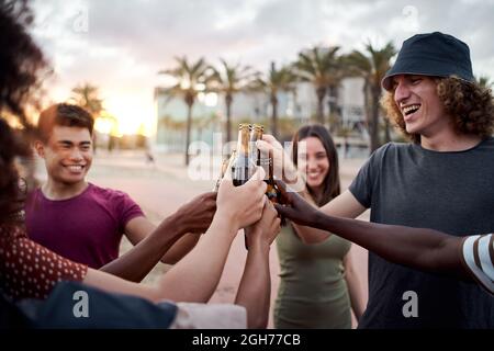 Eine Gruppe junger Menschen mit einem schönen Lächeln toastt den Sonnenuntergang. Glückliche gemischte Rennfreunde, die Spaß haben. Stockfoto