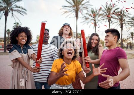 Eine internationale Gruppe junger Menschen feiert draußen mit Konfetti. Konzept der Feier, Party, genießen, fröhlich. Stockfoto