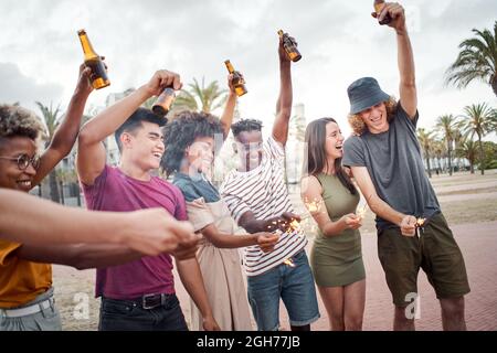 Eine Gruppe von Freunden feiert mit Funkeln und Bieren. Menschen verschiedener Rassen, die eine gute Zeit auf einem Musikfestival haben. Konzept des Sommers, Freundschaft Stockfoto