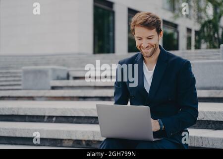 Junger Geschäftsmann sitzt auf der Treppe nutzt Laptop organisiert Treffen online mit Investoren Stockfoto