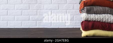 Stapel von gestrickten warmen Kleidern auf Holztisch. Banner. Herbst und Winter Hintergrund. Stockfoto