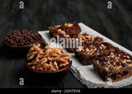 Schokoladenbrownie neben Walnüssen und Pralinen in Tontöpfen Stockfoto