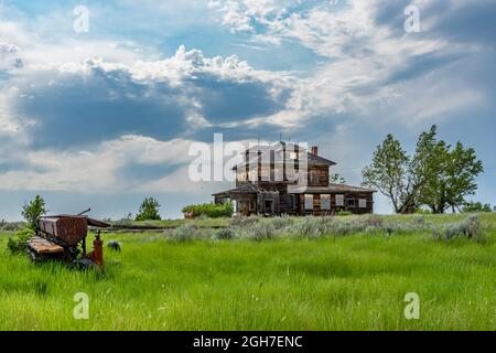 Ein altes, verlassenes Haus auf den Prärien von Saskatchewan mit landwirtschaftlichen Geräten im Vordergrund Stockfoto