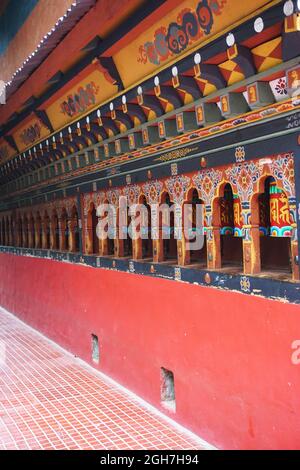 Farbenfrohe, identische Gebetsräder, die in einer Reihe von bemalten Holznischen montiert sind, säumen eine Wand im Thangtong Dewachen Dupthop Nunnery, Thimphu, Bhutan. Stockfoto