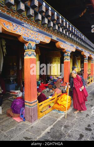 Eine ältere bhutanische Frau in traditioneller Kleidung geht an hell gestrichenen Säulen auf dem Gelände des National Memorial Chörten in Thimphu, Bhutan, vorbei Stockfoto