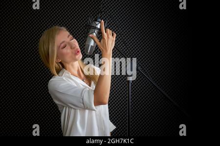 Junge kaukasische Frau singt vor schwarzen Schallschutzwänden. Musiker, die Musik im professionellen Aufnahmestudio produzieren. Stockfoto