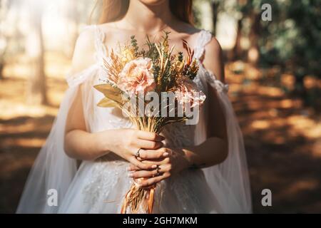 Braut mit weißem Hochzeitskleid im Wald hält bunte und getrocknete Hochzeit Bouquet. . Hochwertige Fotos Stockfoto