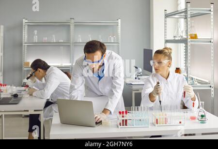 Wissenschaftler forschen an wichtigen Forschungsarbeiten. Eine Frau hält ein Reagenzglas, ein Mann arbeitet an einem Laptop. Stockfoto