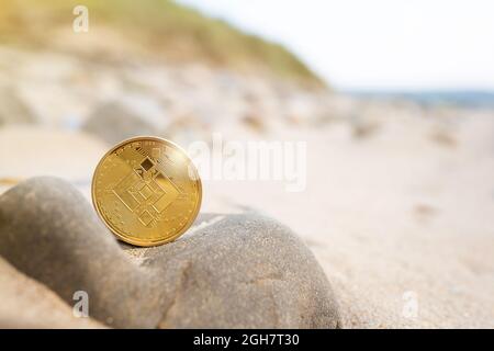 Binance Münze auf Stein mit Strand Hintergrund mit Kopierplatz. Einzelne goldene Krypto-BNB-Outdoor-Banner in warmen Tönen. Umweltauswirkungen von Bergbau Kryptowährung, Sommer, Urlaub Konzept. Stockfoto