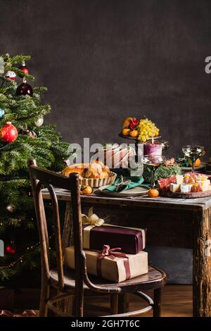 Stilvolles Tischdekable für das weihnachtsessen der Familie mit weihnachtsbaum auf dem Hintergrund und Geschenken auf dem Stuhl. Stockfoto