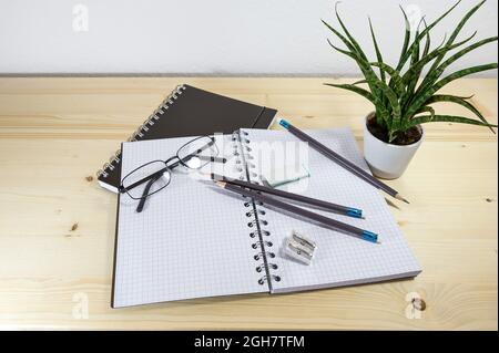 Büro- oder Schreibtisch mit offenem Spiralheftchen, Bleistiften, Brillen und Zubehör auf einem Holztisch, Kopierraum, ausgewählter Fokus, enge Schärfentiefe Stockfoto