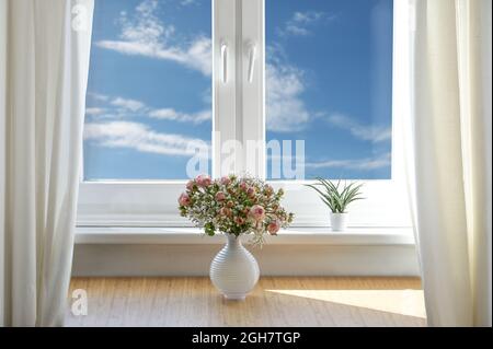 Romantischer Blumenstrauß mit Rosen und Babyluft in einer weißen Vase auf einem Tisch am Fenster mit blauem Himmel und Wolken, Kopierraum, ausgewählter Fokus Stockfoto