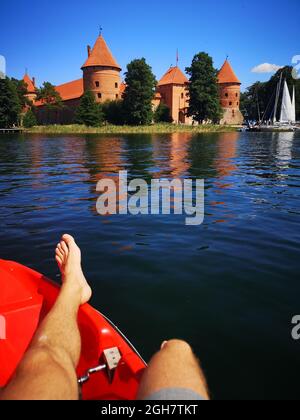 Vertikale Aufnahme des weiblichen Beins am Ufer mit Trakai-Schloss im Hintergrund an einem sonnigen Tag Stockfoto