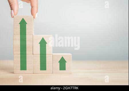 Holzblock, der von Hand als Treppenhaus mit grünem Pfeil nach oben stapelt. Verkürzte Hände Der Person Stapeln Von Holzblöcken Auf Den Tisch. Karrierepfad für Stockfoto