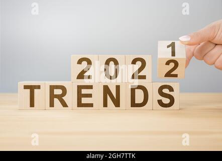 Trends 2022 Blocks. 2022 Trends Neujahr Symbol. Frau dreht einen Holzwürfel und ändert die Worte Trends 2021 zu Trends 2022. Drehen des hölzernen Würfelblocks Stockfoto