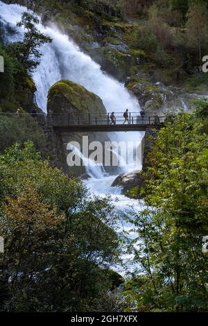 Touristen überqueren eine Brücke vor einem Wasserfall am Briskdal Gletscher, Jostedal Gletscher Nationalpark, Norwegen, Europa Stockfoto