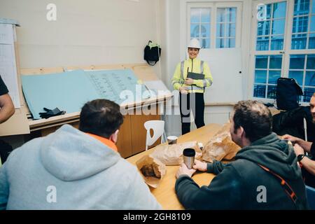 Lächelnde Ingenieurin, die im Büro mit männlichen Bauarbeitern diskutiert Stockfoto