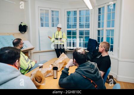 Eine Bauunternehmerin mit digitalem Tablet diskutiert mit männlichen Kollegen während der Planung im Büro Stockfoto