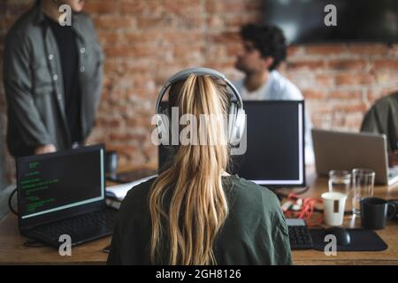 Eine Hackerin mit Kopfhörern, die im Büro über den Computer arbeitet Stockfoto