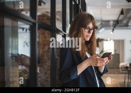 Junge Unternehmerin Textnachrichten auf dem Smartphone in Startup-Unternehmen Stockfoto