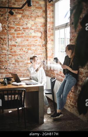 Glückliche weibliche Kollegen, die im Büro Kaffee trinken Stockfoto
