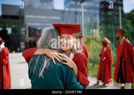 Porträt einer fröhlichen Universitätsstudentin, die Mutter im Freien umarmt, Abschlusskonzept. Stockfoto