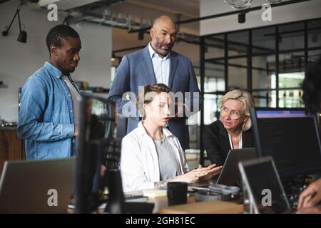 Eine Geschäftsfrau erklärt männlichen und weiblichen Anlegern den Laptop im Büro Stockfoto