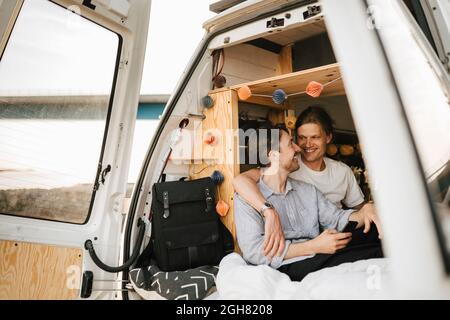 Lächelnde männliche Freunde, die sich während der Sommerferien im Campingbus angusten Stockfoto