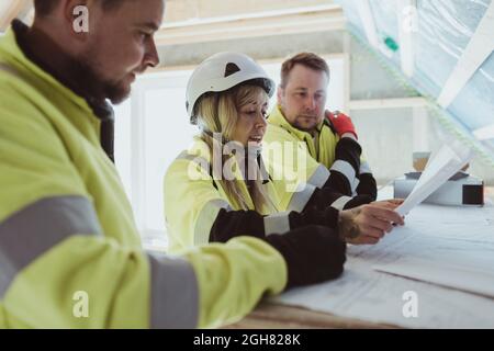 Eine Bauunternehmerin diskutiert mit männlichen Kollegen auf der Baustelle über den Grundriß Stockfoto