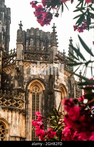 Gotisches altes Kloster von Batalha am bewölkten Tag in rosa Oleanderblüten im Vordergrund - Nerium Oleander, Batalha, Portugal, Vertical, Selective Stockfoto