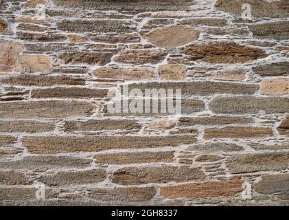 Alte natürliche braune Steinwand mit grauem Zementhintergrund. Unregelmäßiges Mauerwerk Stockfoto