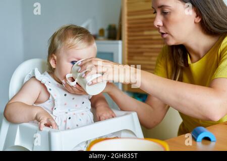 Mutter füttert Tochter mit Baby-Formel in Tasse. Gesunde Ernährung. Kinderbetreuung Stockfoto