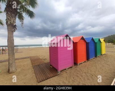 Holzhütten in verschiedenen Farben im Sand des Strandes von Oropesa del Mar an einem bewölkten Tag in Castellón, Spanien. Europa. Horizontale Fotografie. Stockfoto