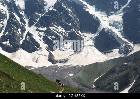 Eine Gruppe von Wanderern mit Rucksäcken wandern entlang einer Bergkette vor dem Hintergrund verschneiter Berge. Das Konzept der Reise zum Berg Stockfoto