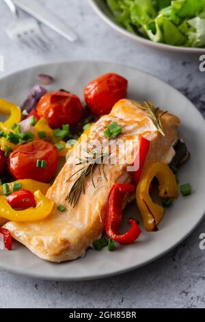 Gebackenes rotes Fischfilet Arctic Saibling auf einem Teller mit Gemüse, Salat in einer Schüssel mischen, leckeres herzhaftes gesundes Abendessen Stockfoto